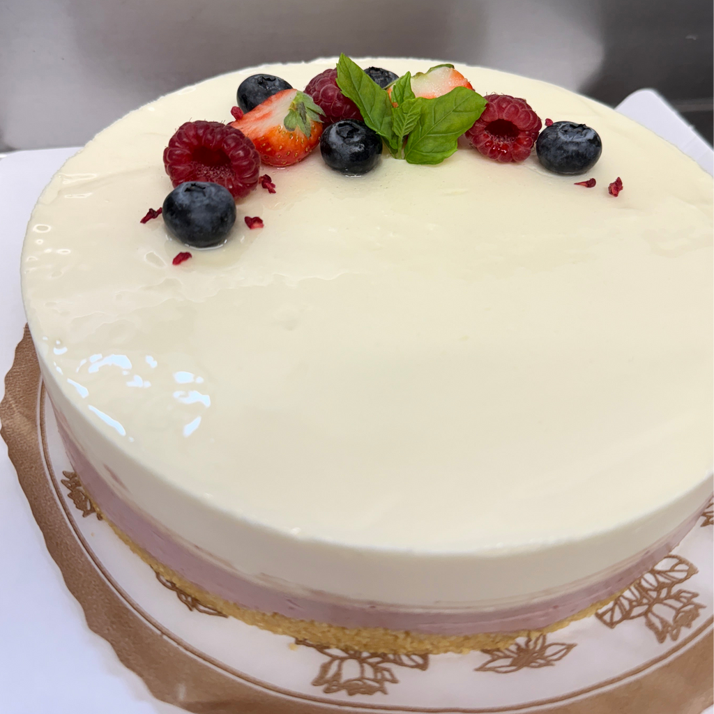 Pyöreä kakku, jossa on kaksi kerrosta valkoinen ja vaaleanpunainen moussekerros. Koristeena minttua, mustikkaa, mansikkaa ja vadelmaa.